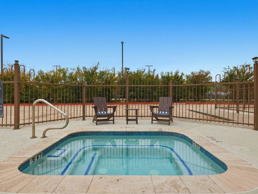 A swimming pool with two lounge chairs, a metal fence, and trees in the background.