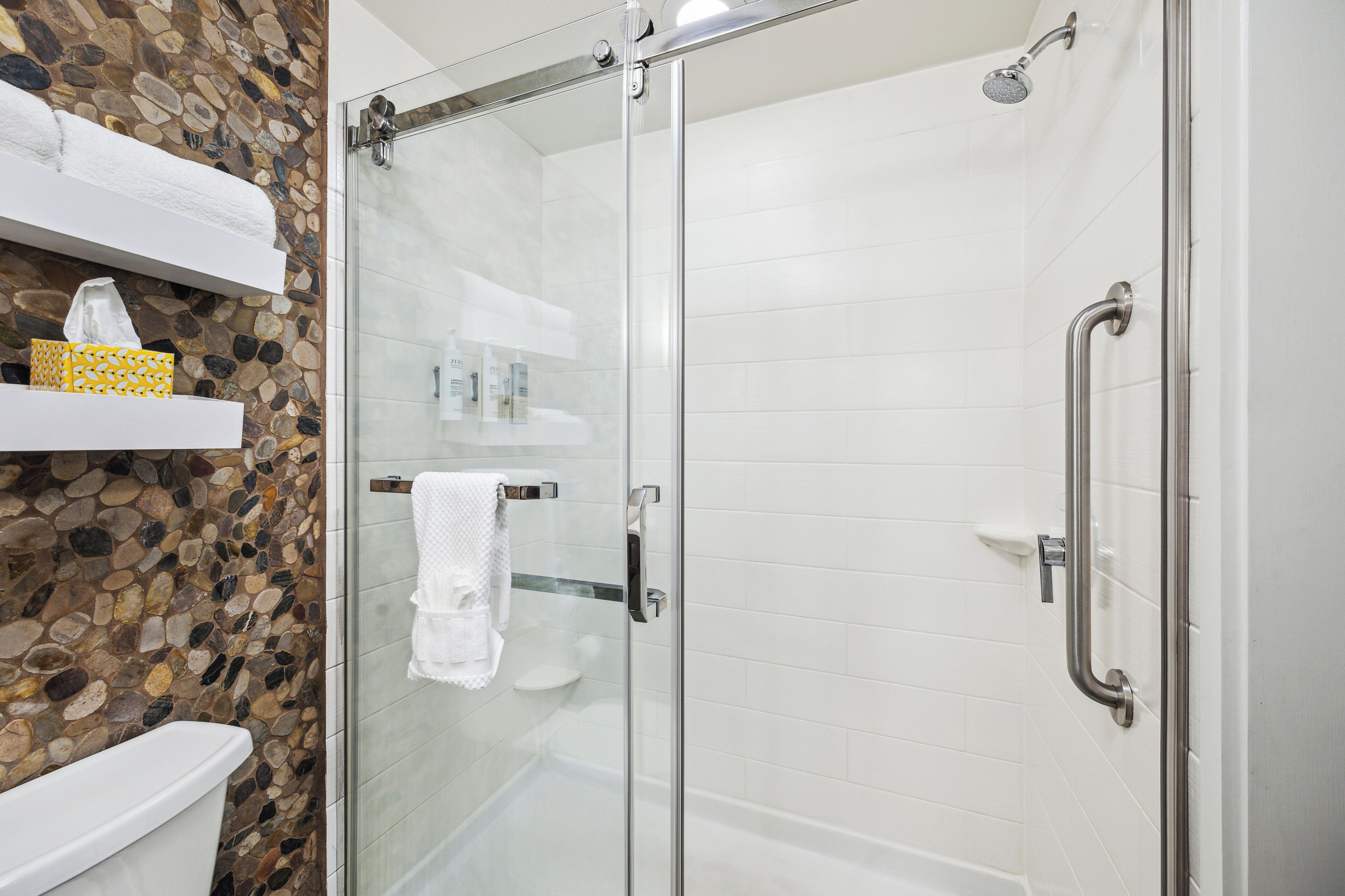 A modern bathroom with a glass-enclosed shower, white tiles, a stone mosaic backsplash, and a white toilet.