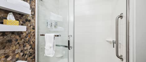 Un baño moderno con ducha de mampara de vidrio, azulejos blancos, un salpicadero de mosaico de piedra y un inodoro blanco.