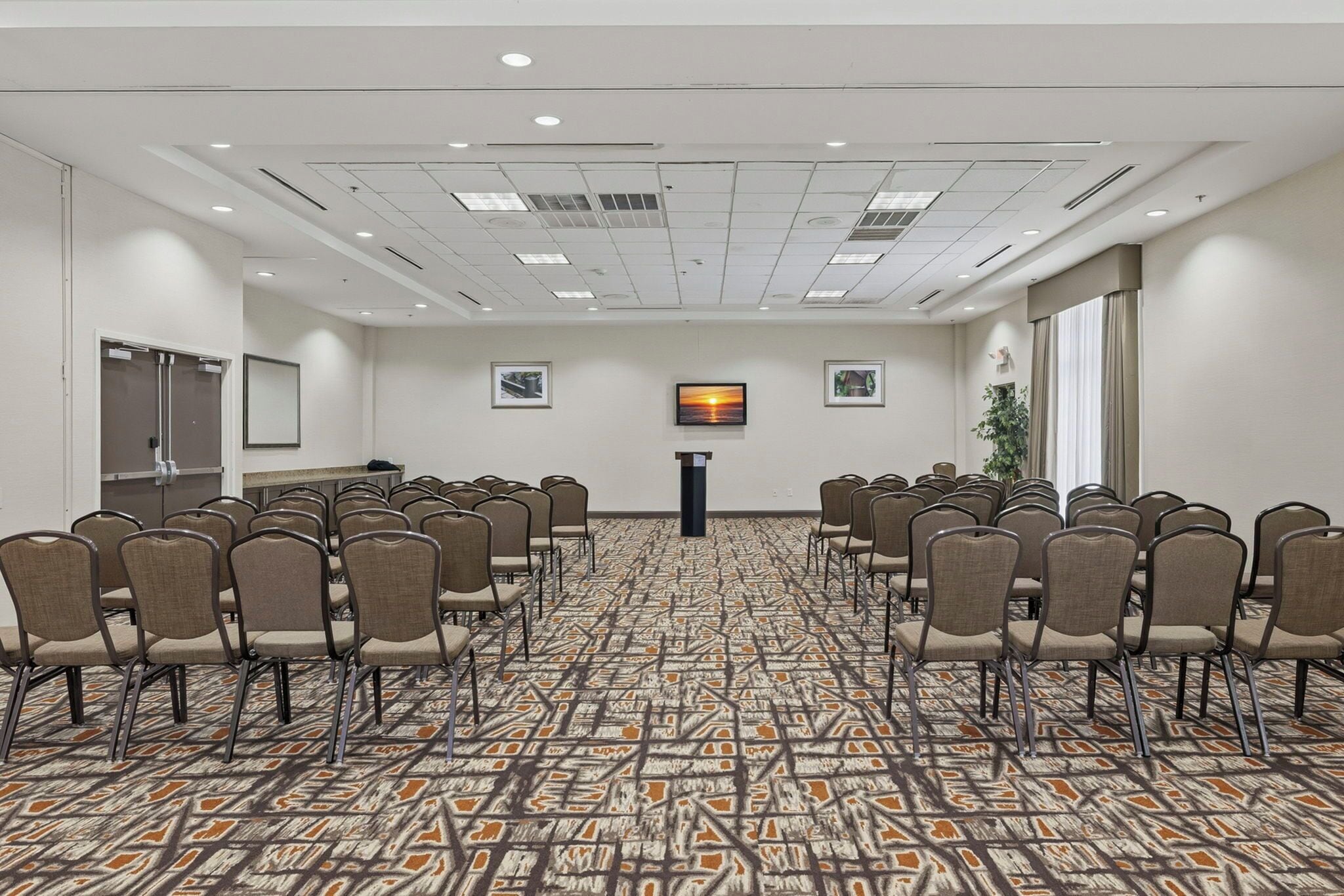 Una sala conferenze con file di sedie rivolte a un podio, un tappeto decorato e quadri appesi alle pareti.