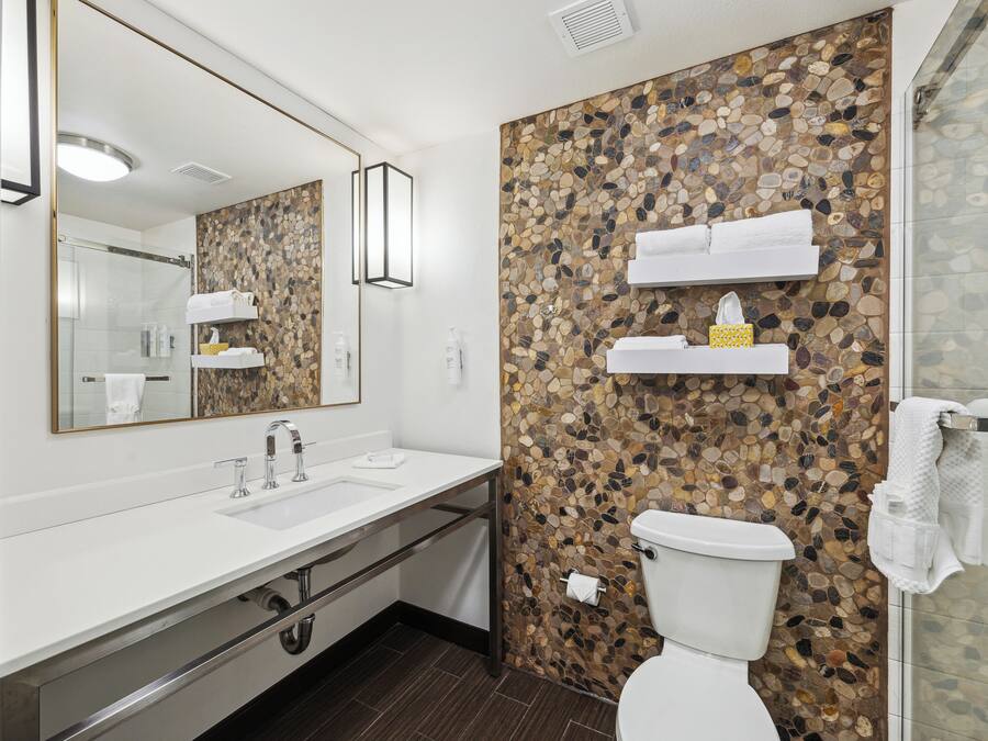 A modern bathroom with a white sink, a large mirror, a toilet, and a shower area.