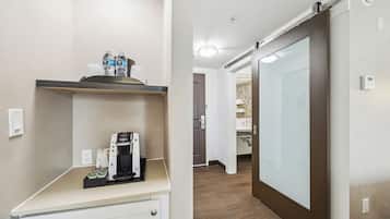 A hotel room with a kitchenette area featuring a coffee maker, water bottles, and a coffee pod machine.