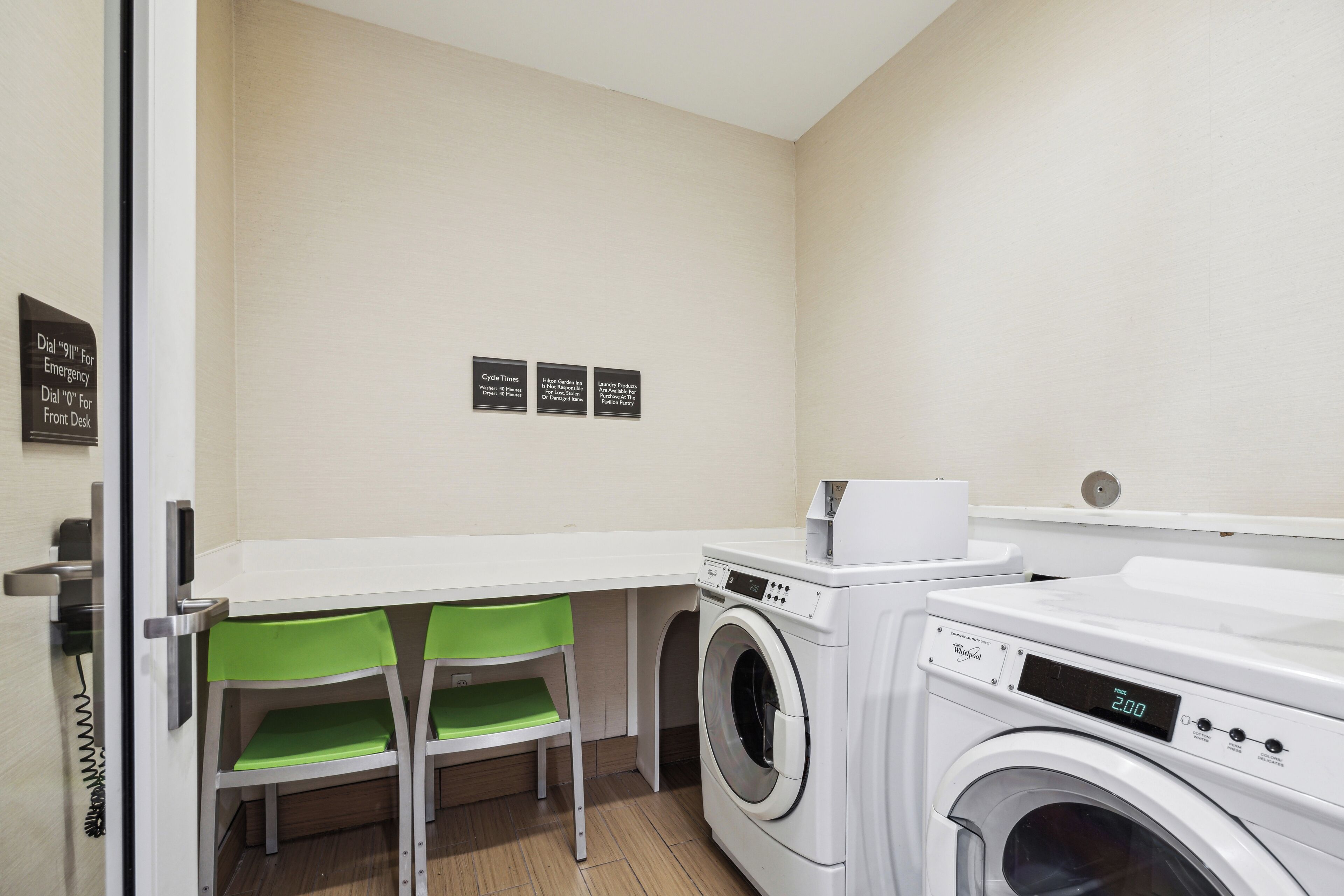 A laundry room with a washing machine, two green chairs, and a white table.