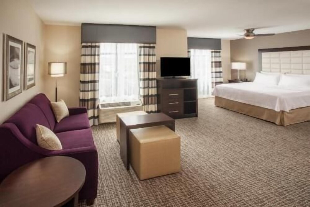 A hotel room with a bed, a sofa, a TV, a desk, and a window with curtains.