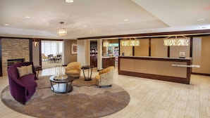 A hotel lobby with a reception desk, seating area with armchairs, a coffee table, and a fireplace. - Homewood Suites by Hilton Munster (Munster)