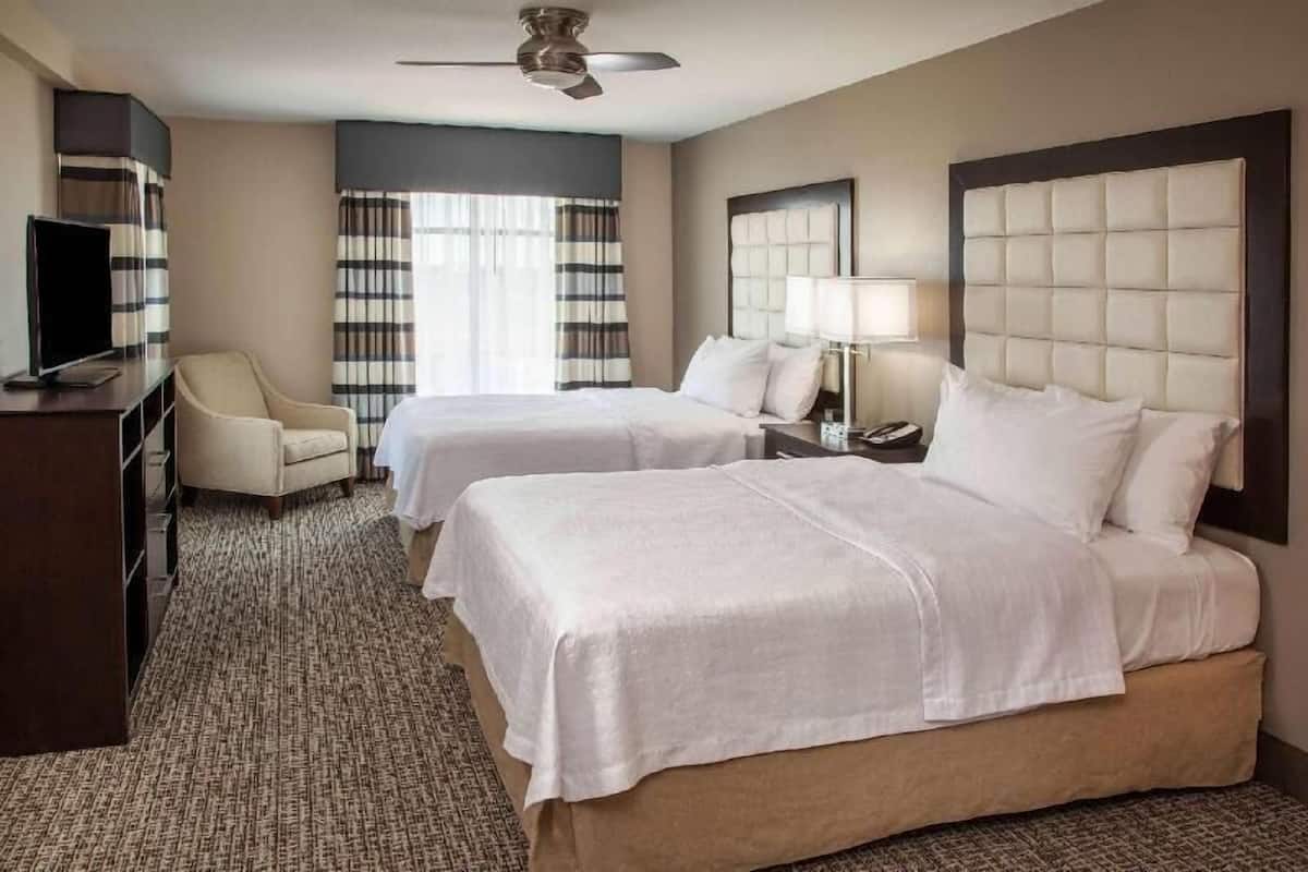 A hotel room with two beds, a TV, a desk, and a chair.