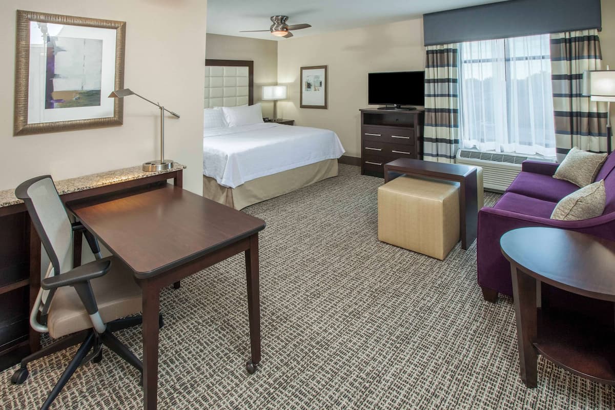 A hotel room with a bed, desk, chair, sofa, and TV.