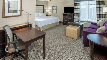 Habitación de hotel con cama, escritorio, silla, sofá y televisor.