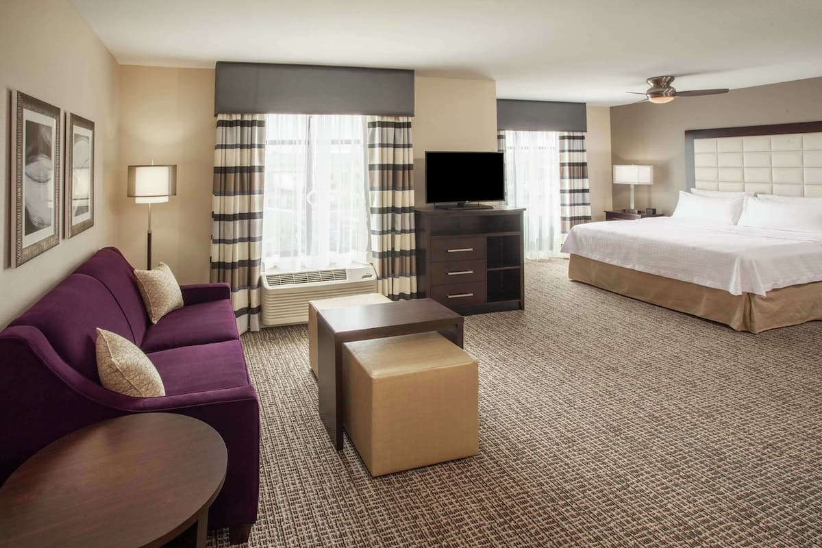A hotel room with a bed, a sofa, a TV, a desk, and a window with curtains.