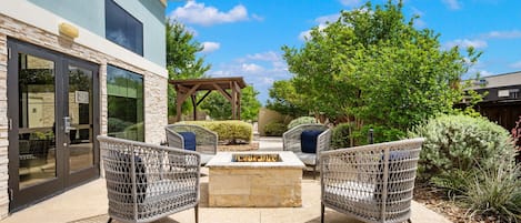 Un patio con sillas de mimbre, un hogar de piedra y una pérgola.