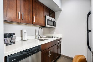 A compact kitchen with wooden cabinets, a microwave, a dishwasher, and a sink. - Homewood Suites By Hilton New Braunfels (New Braunfels)