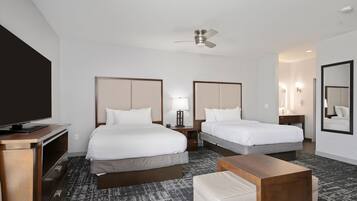 A hotel room with two beds, a TV, a ceiling fan, a desk, and a mirror.