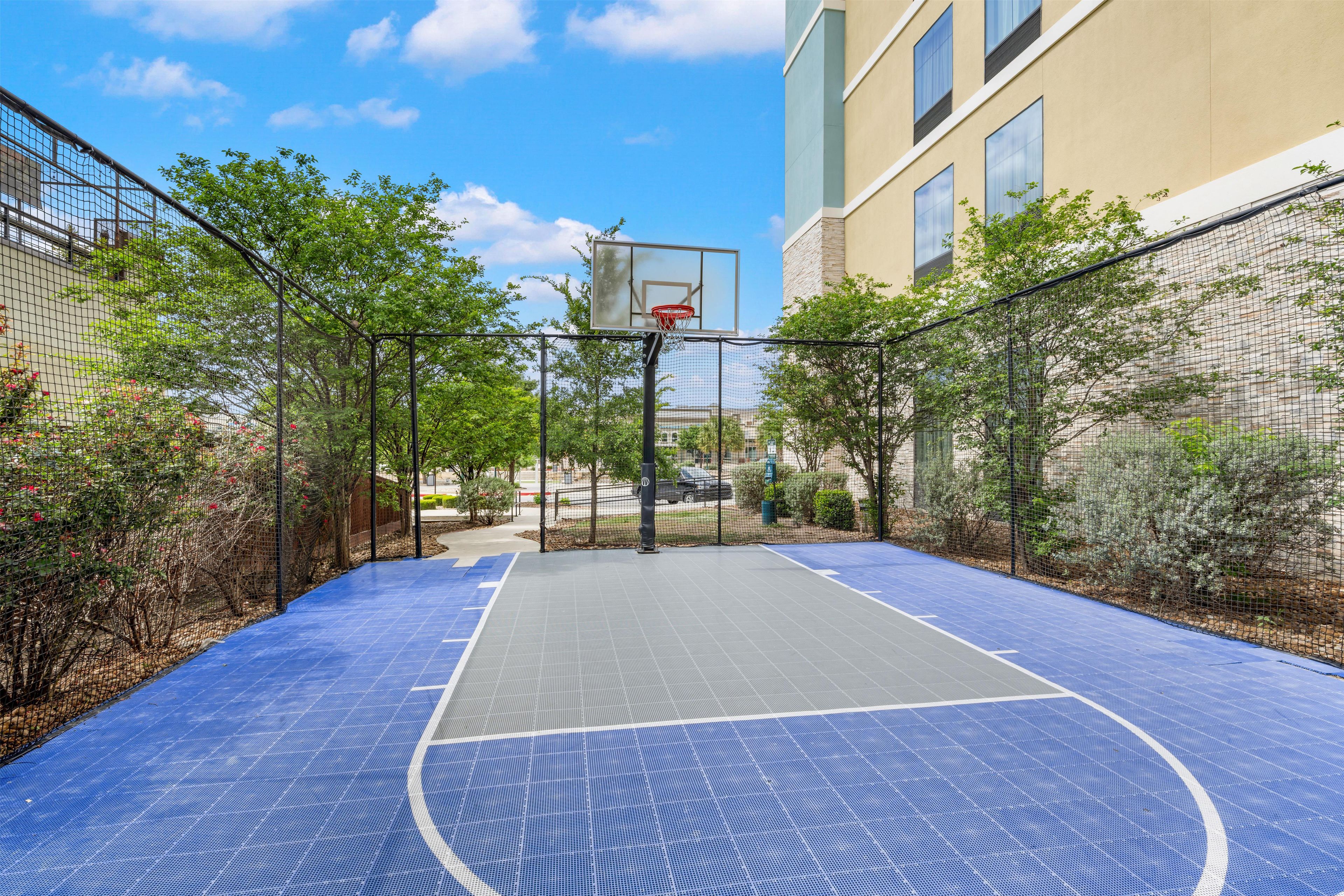 Ein Basketballplatz im Freien mit Netz, umgeben von Bäumen und einem Gebäude.