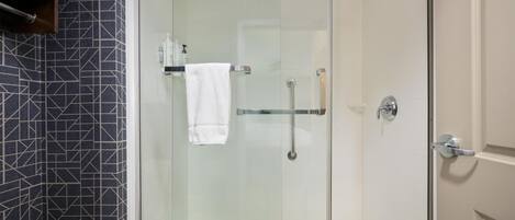 A glass-enclosed shower with a white towel hanging on a rack, a glass shelf with toiletries, and a patterned wall.