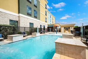 A swimming pool with lounge chairs and a covered area, surrounded by a building with multiple windows and a stone facade. - Homewood Suites By Hilton New Braunfels (New Braunfels)