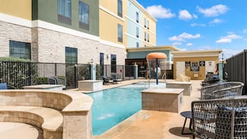 A pool area with lounge chairs, a covered seating area, and a building with multiple windows and a stone facade.