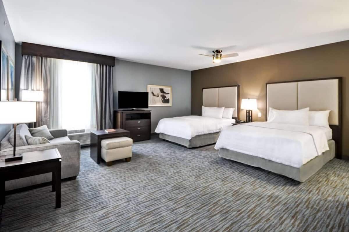 A hotel room with two beds, a sofa, a TV, a desk, and a ceiling fan.