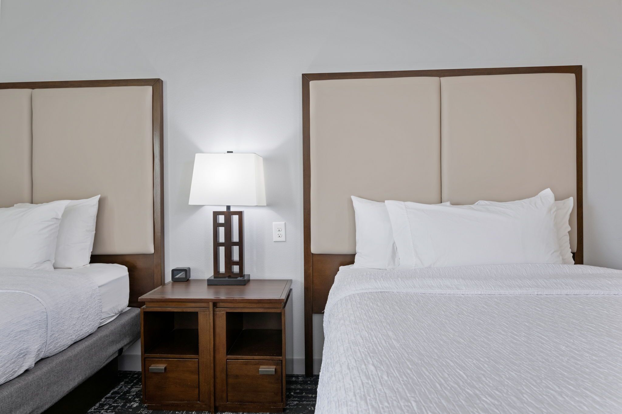 A hotel room with two beds, a nightstand with a lamp, and a small table.