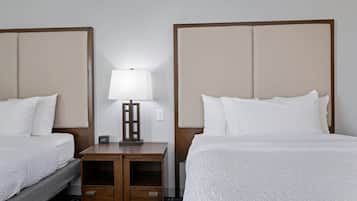 A hotel room with two beds, a nightstand with a lamp, and a small table.