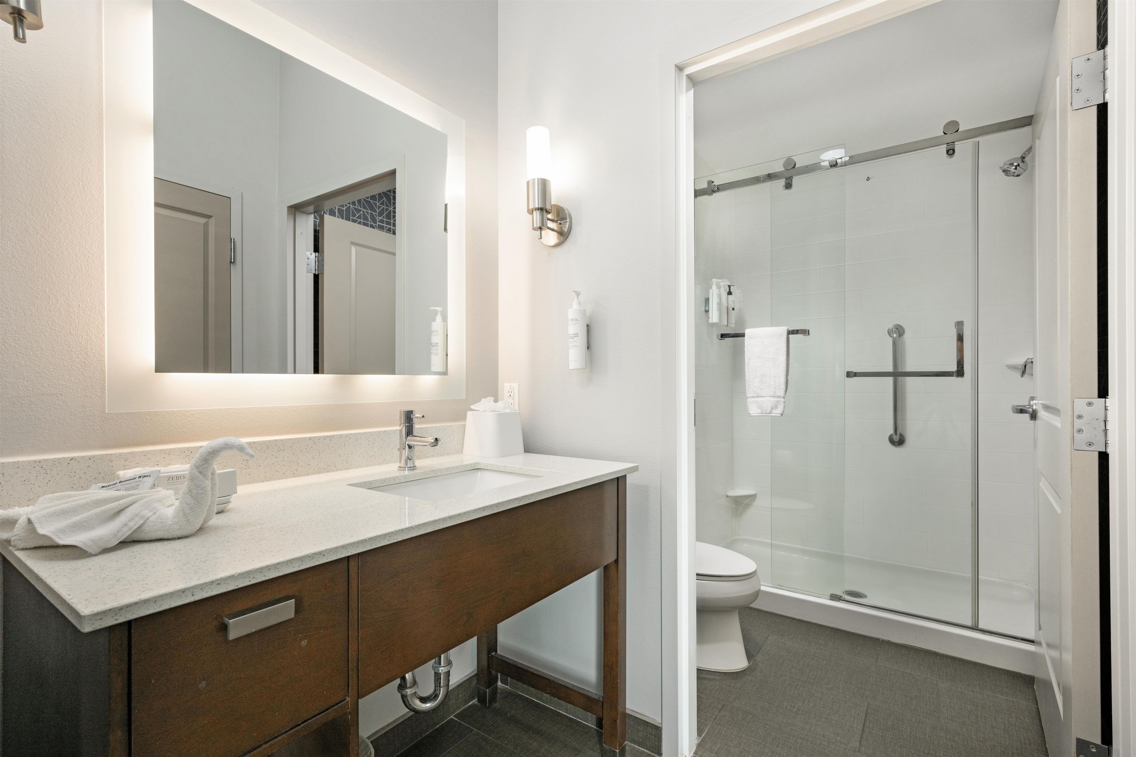 A bathroom with a mirror, sink, vanity, and shower.