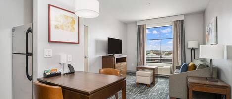 A hotel room with a dining table, chairs, a sofa, a TV, a desk, and a window with a view.