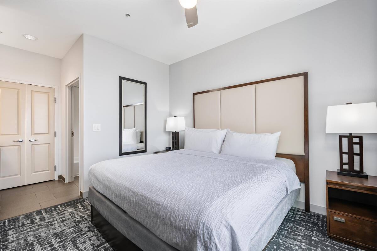 A hotel room with a large bed, a nightstand, a mirror, and a door.