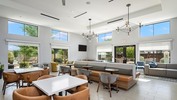 A spacious indoor area with a seating arrangement, a dining table, and a large window providing a view of the outdoors. - Homewood Suites By Hilton New Braunfels (New Braunfels)