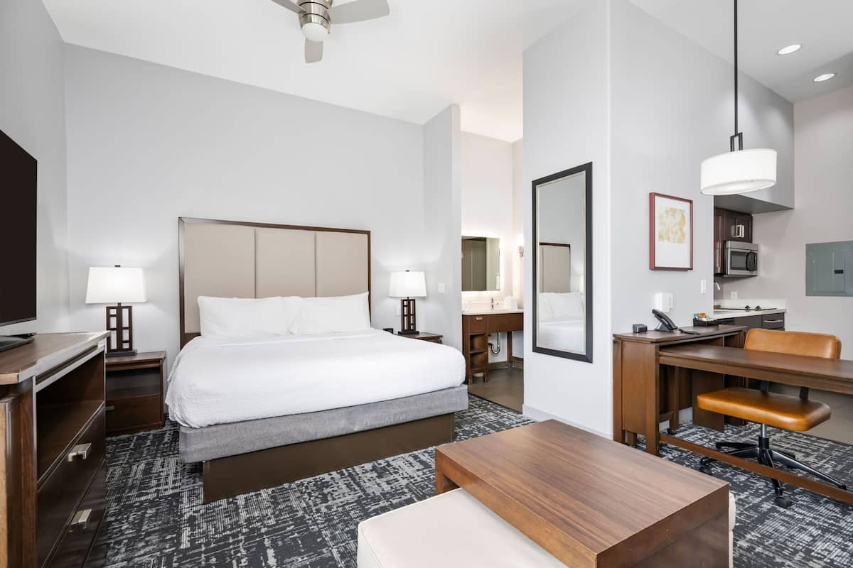 A hotel room with a bed, desk, chair, lamp, and a large mirror.