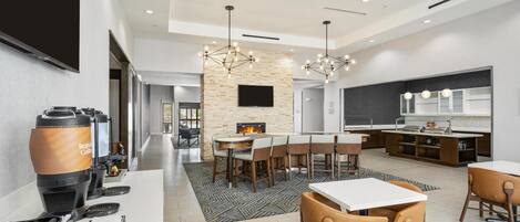 A modern kitchen with a flat-screen TV, a coffee machine, and a dining area with chairs and a table.