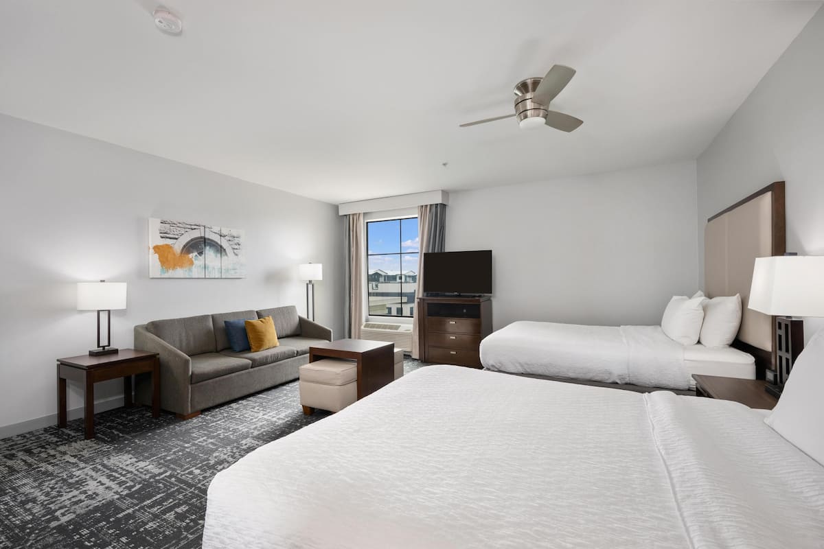 A hotel room with a bed, a sofa, a TV, a ceiling fan, and a window with curtains.