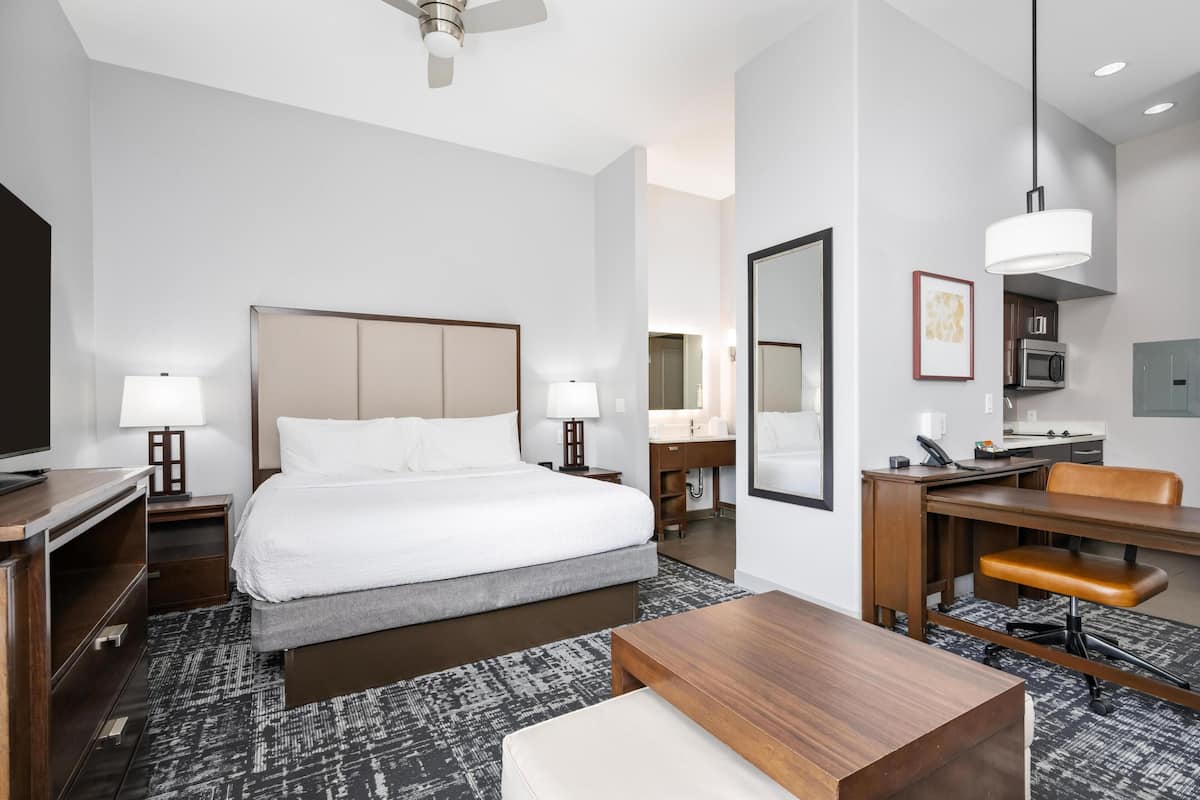 A hotel room with a bed, desk, chair, lamp, and a television.