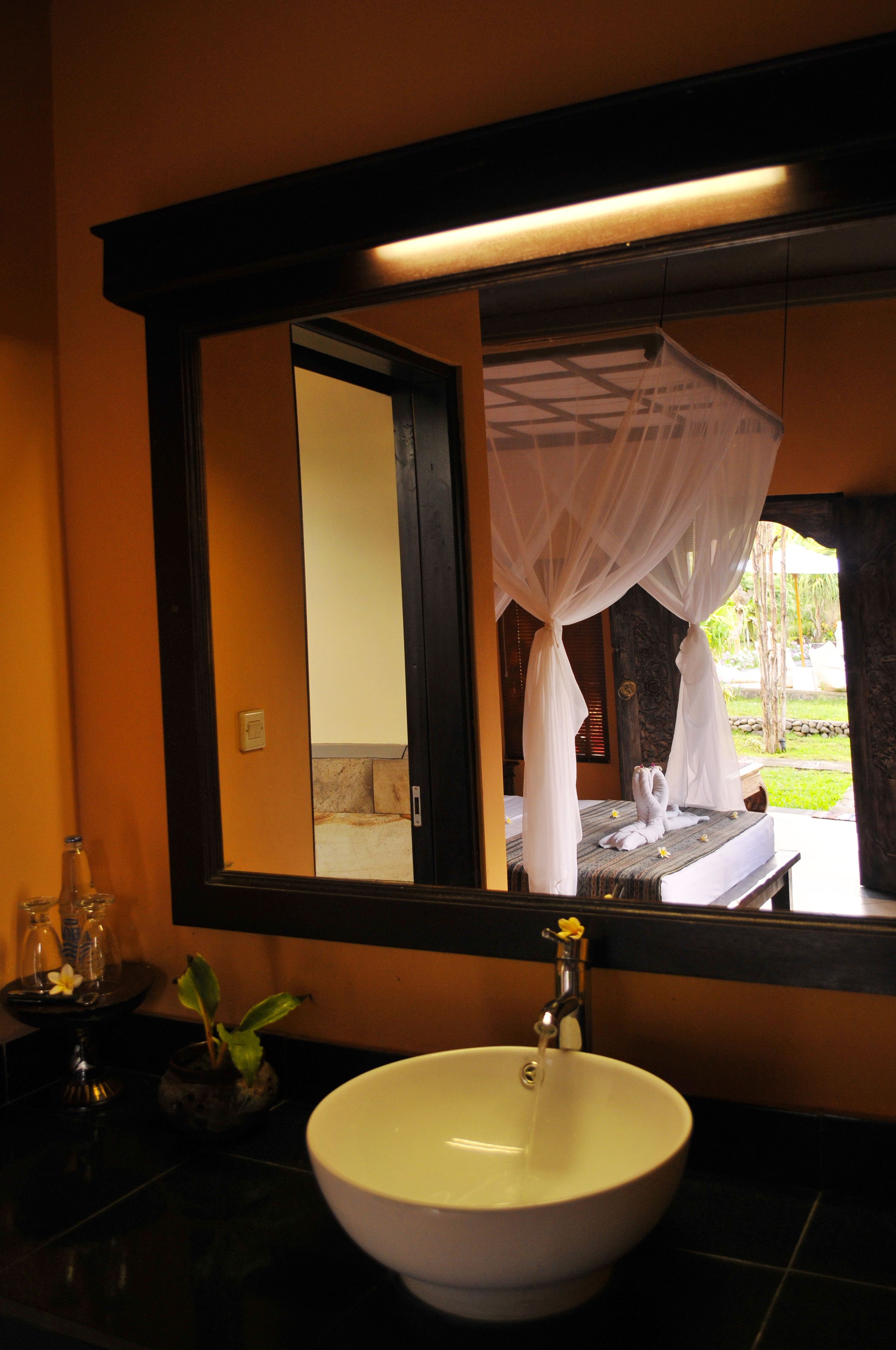 A bathroom with a large mirror, a white sink, and a bed with a canopy.