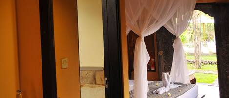 A bathroom with a large mirror, a white sink, and a bed with a canopy.
