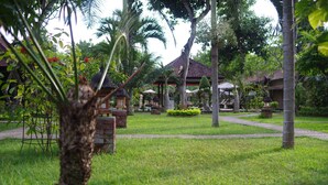A lush garden with palm trees, a gazebo, and a thatched-roof building. - Tirta Sari Bungalows & Spa (Pemuteran)