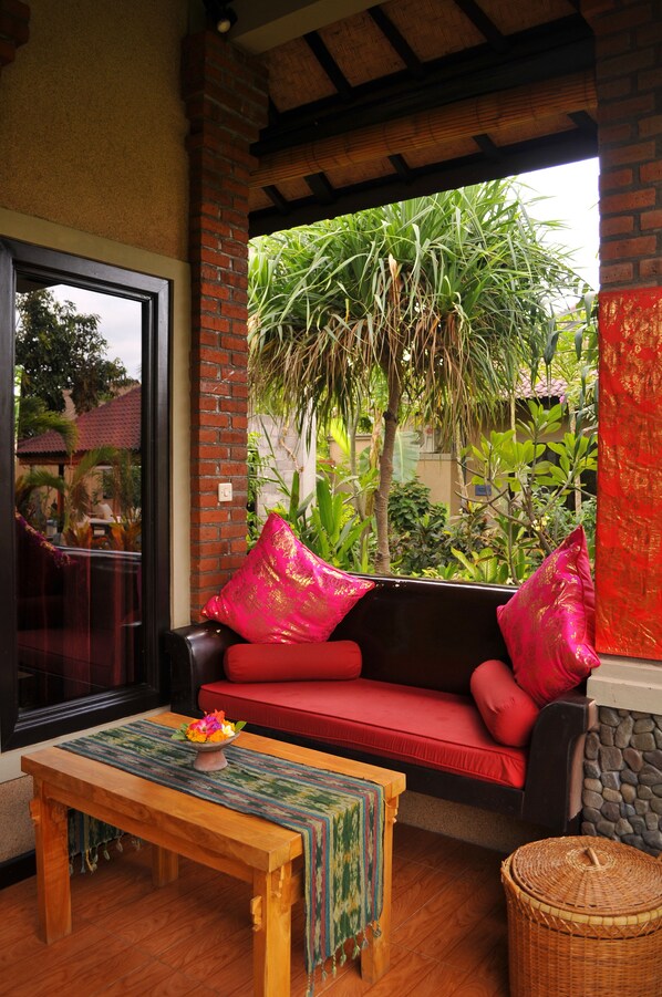 A cozy indoor seating area with a red sofa, a wooden table with a woven table runner, and a wicker basket. - Tirta Sari Bungalows & Spa (Pemuteran)