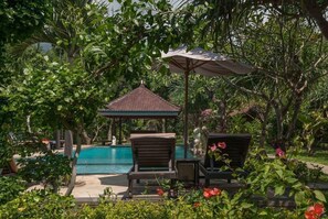 A pool area with lounge chairs, a gazebo, and lush greenery. - Tirta Sari Bungalows & Spa (Pemuteran)