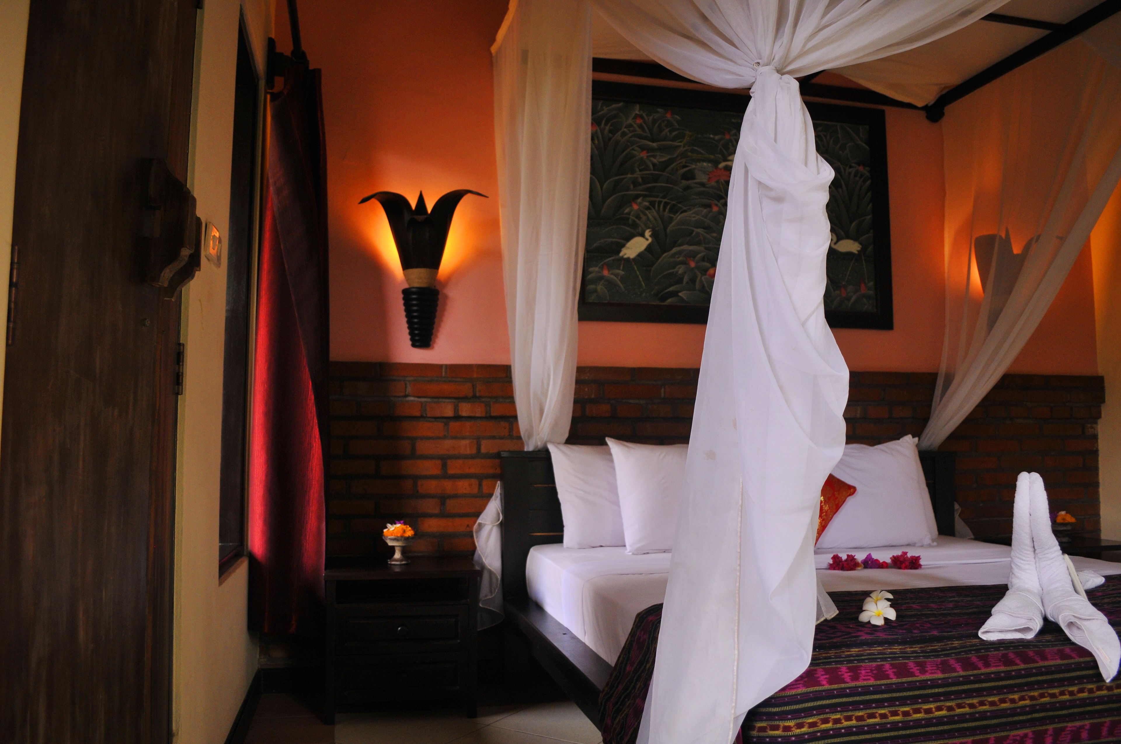 A bedroom with a bed, a nightstand, a wall-mounted light, and a painting.