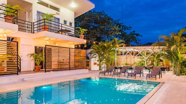 Un hotel moderno con piscina, mobiliario exterior y plantas en macetas.
