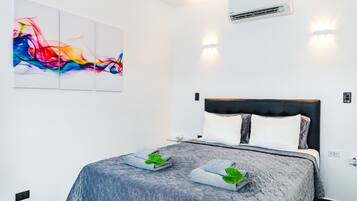 A modern hotel room with a large bed, a colorful abstract painting, and a wall-mounted air conditioner.
