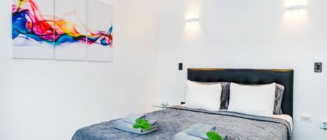 Quarto de hotel moderno com uma cama grande, um quadro abstrato colorido e um ar condicionado fixado na parede.
