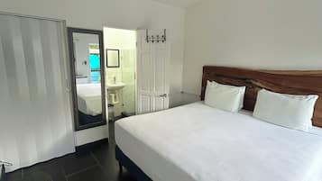 A hotel room with a bed, a ceiling fan, a bathroom with a sink and mirror, and a door leading to another room.