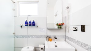 Un baño moderno con un lavabo blanco, un espejo, un secador de pelo y artículos de aseo en un estante.