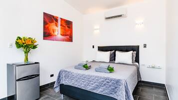 Quarto moderno com cama, geladeira, ar condicionado fixado na parede e uma grande pintura abstrata.