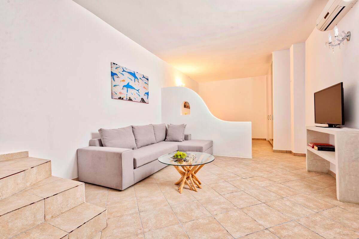 A modern living room with a sofa, a glass coffee table, a TV, and a staircase.