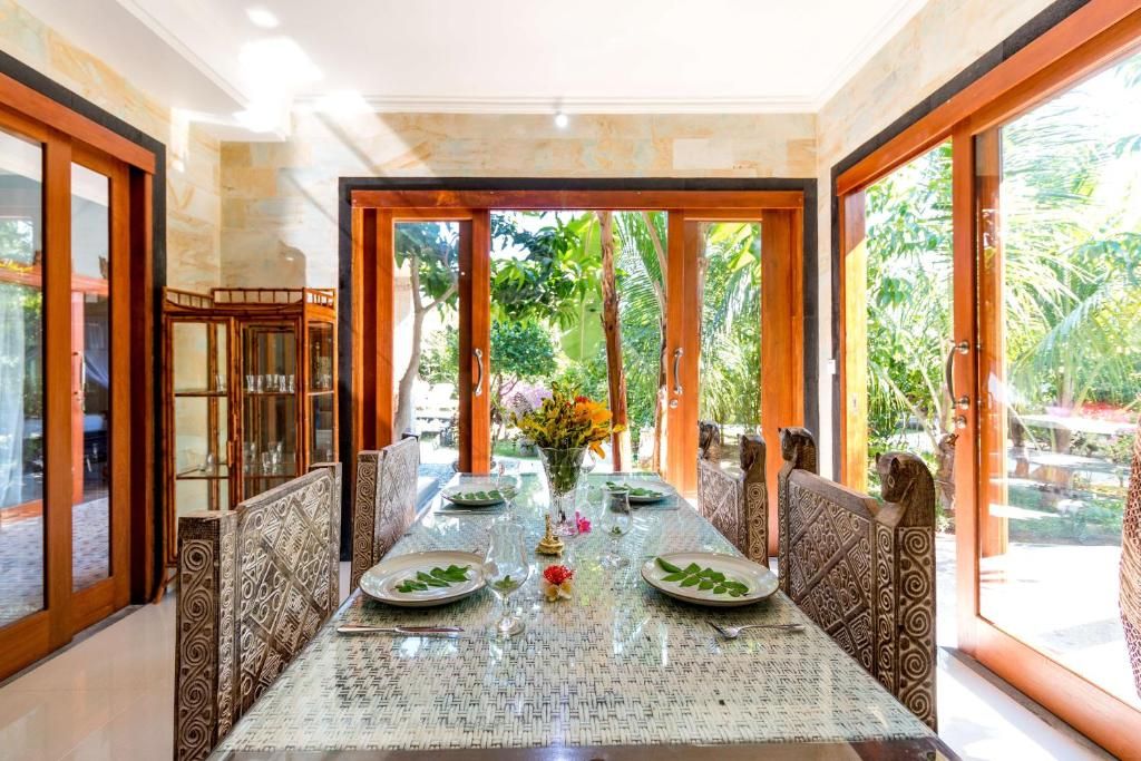 A dining area with a glass table, chairs with patterned upholstery, and a view of greenery outside.