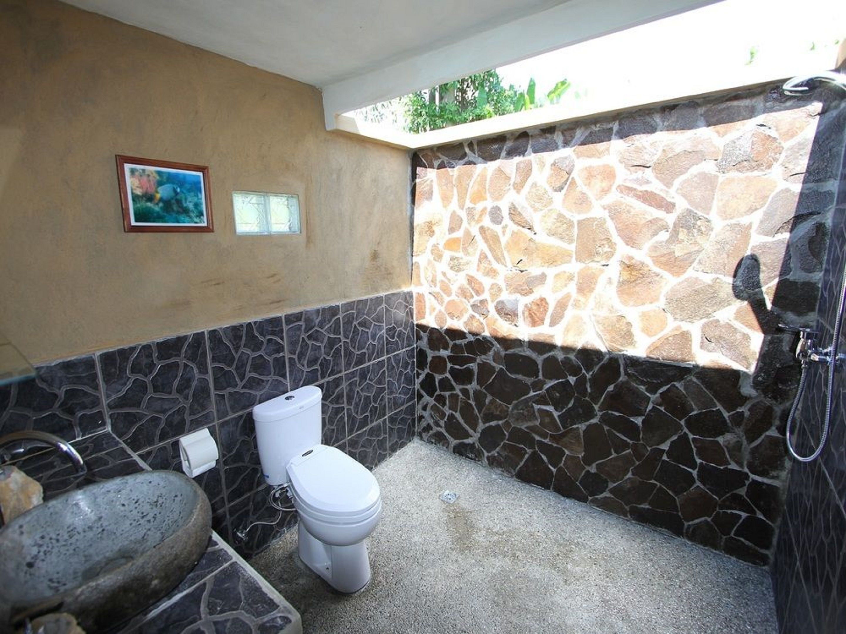 Une salle de bain avec un mur en pierre, des toilettes, un lavabo et une douche.