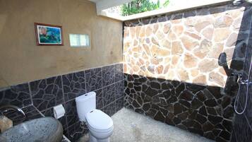 Une salle de bain avec un mur en pierre, des toilettes, un lavabo et une douche.