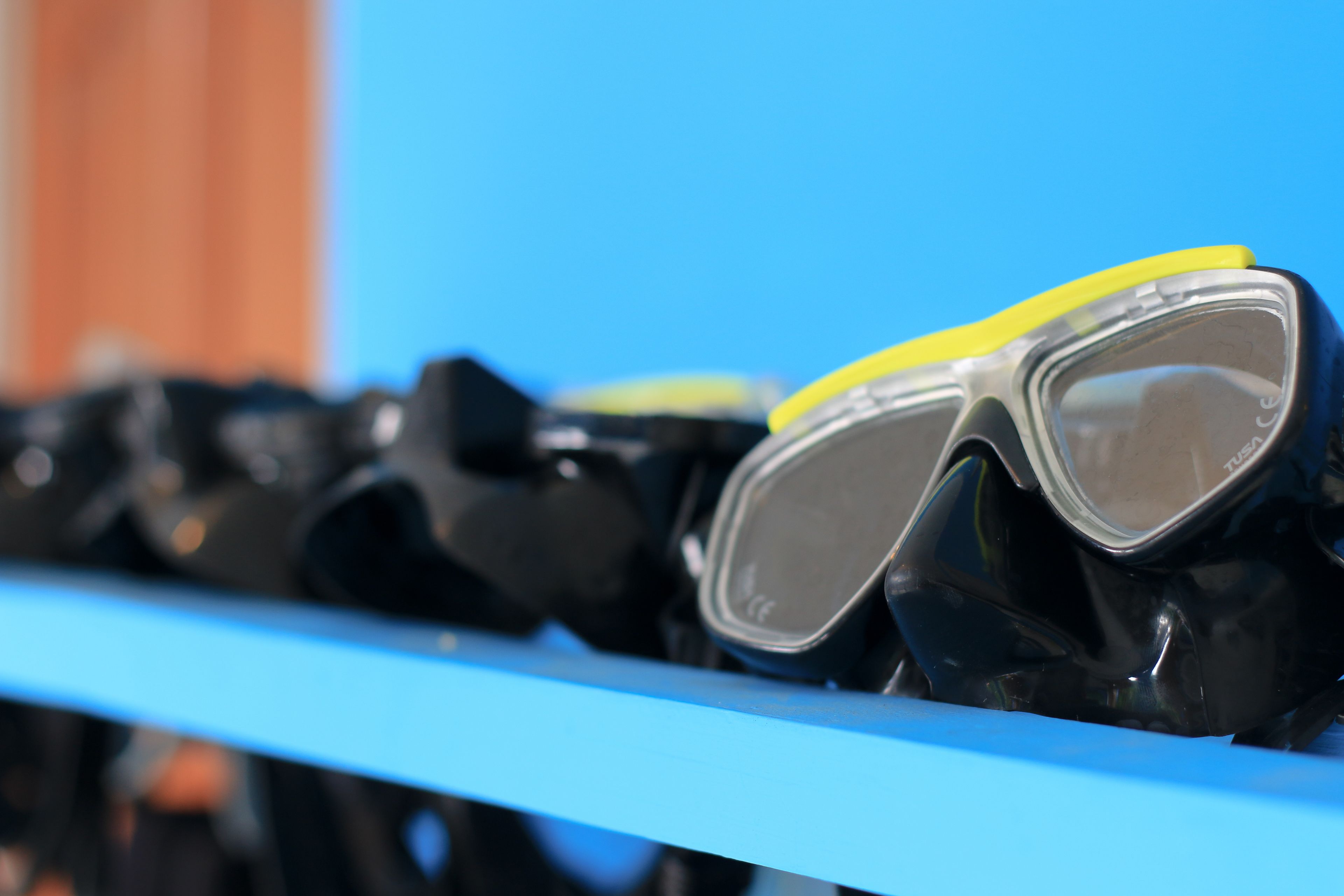 A row of black diving masks with yellow trim on a blue shelf.
