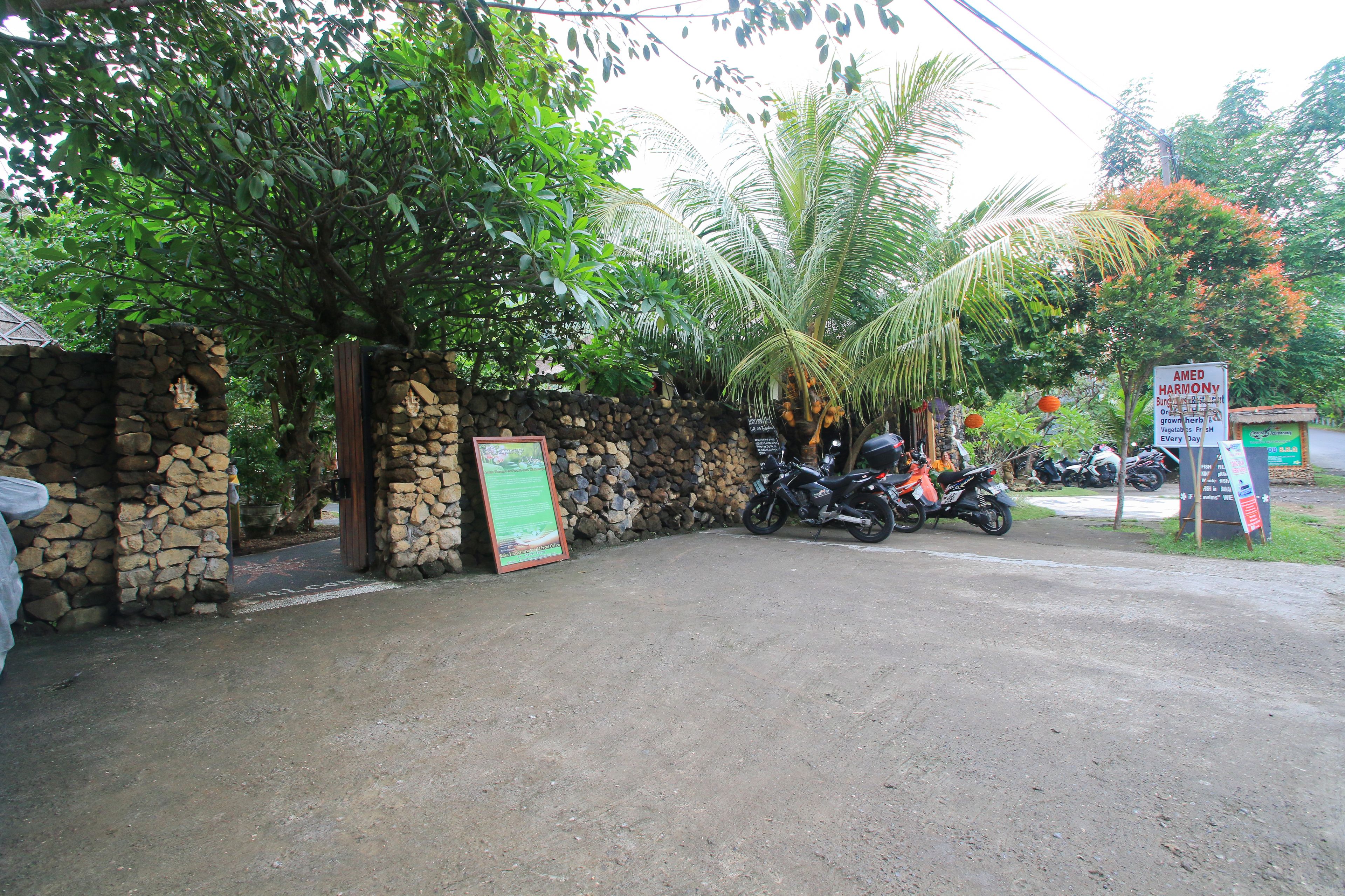 Une entrée en pierre, avec un mur d’enceinte, une enseigne, des motos garées et une végétation luxuriante.