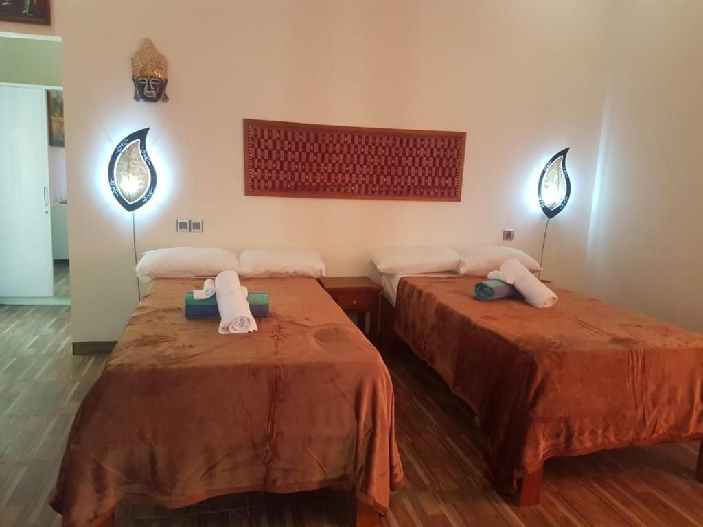 Une chambre d’hôtel avec deux lits, chacun recouvert d’une couverture marron et agrémenté d’oreillers, un panneau décoratif fixé au mur et deux appliques murales.